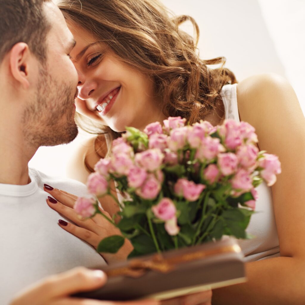Couple embracing, about to kiss holding bouquet of pink flowers.
