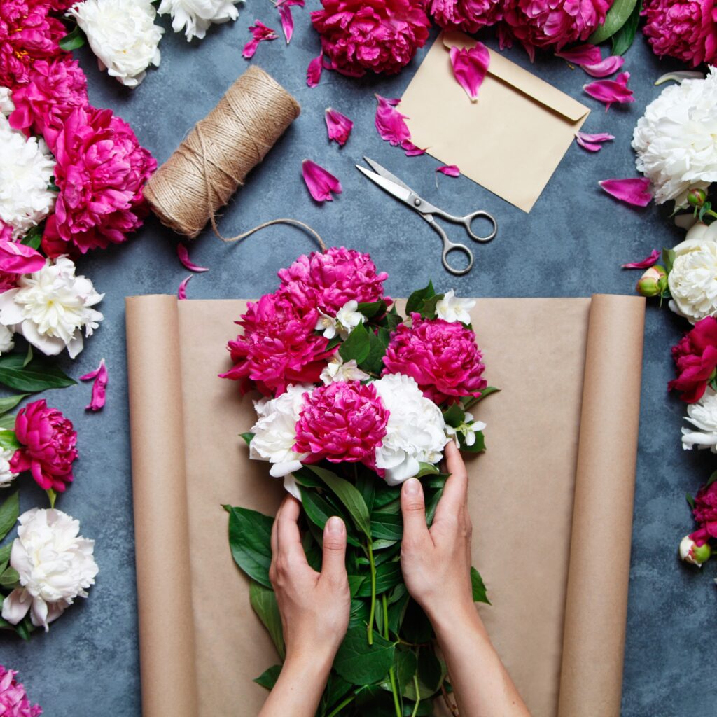Overview of hands making a flower arrangement, with scissors, envelope and string.