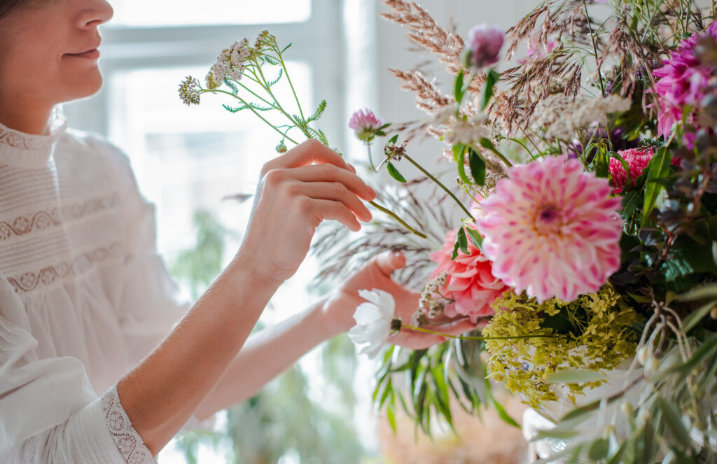 Woman adding to large flower arrangement, Focus on her hands, with face cut off.